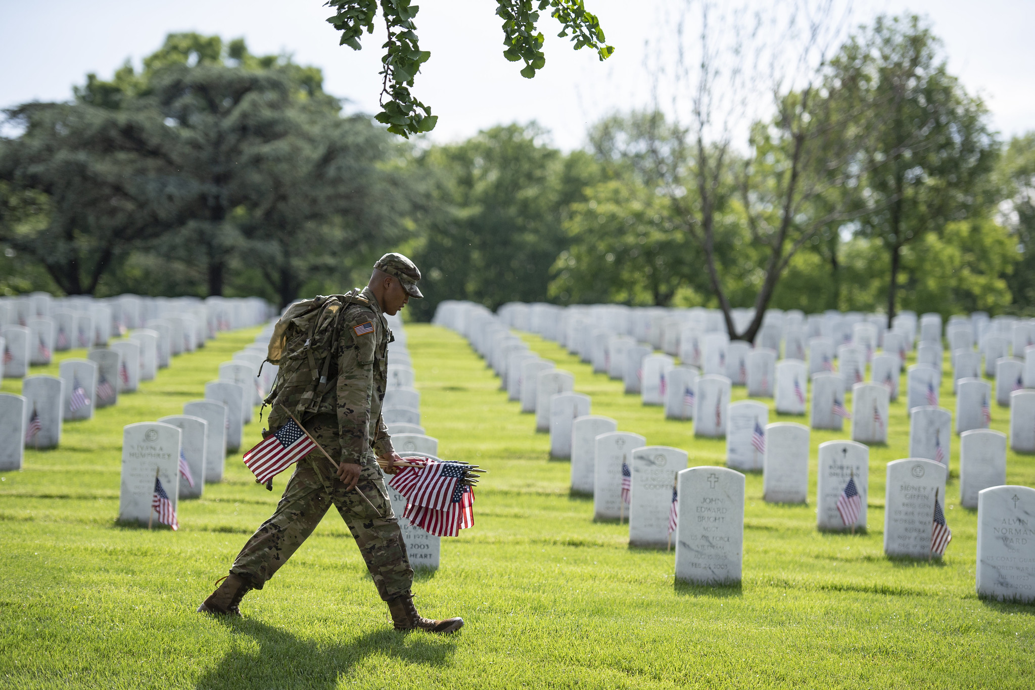 A uniformed soldier places American flags in front of gravestones at Arlington National Cemetery, for Memorial Day