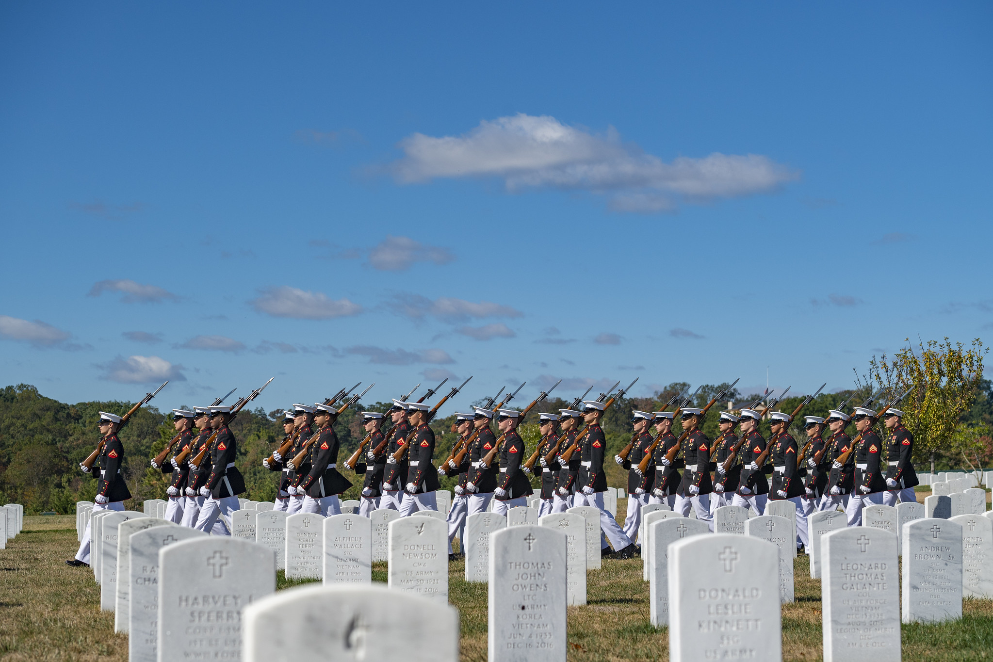 Uniformed Marines march at a military funeral, among gravesites at Arlington National Cemetery