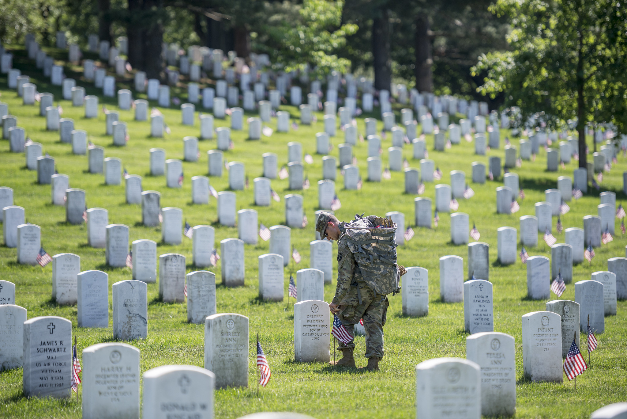 A uniformed soldier places American flags in front of gravesites at Arlington National Cemetery