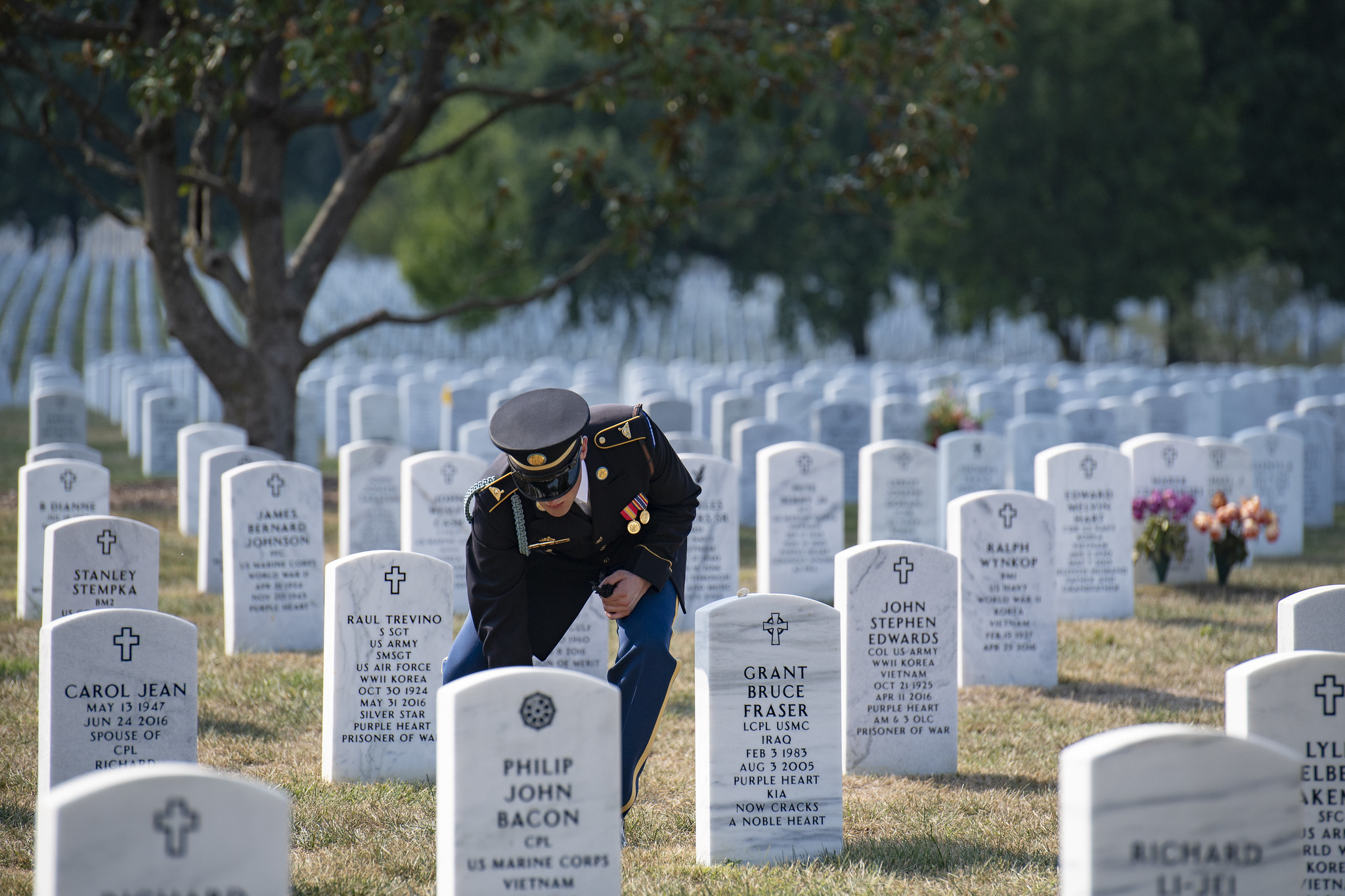 A uniformed soldier kneels before a gravestone at Arlington National Cemetery