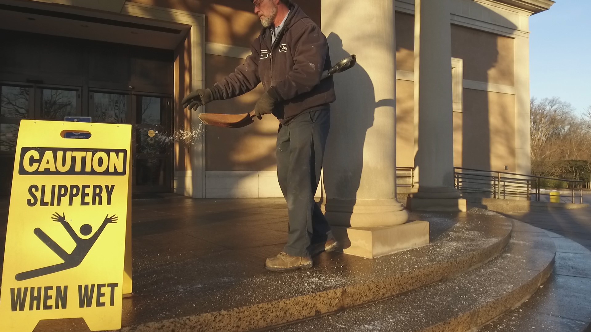 An Arlington National Cemetery employee removes snow and ice in front of the Welcome Center, and a sign reminds visitors of slipping hazards